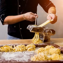 Chef rolling dough with a pasta machine. Pasta maker machine. Homemade italian style cuisine. Restaurant. Background